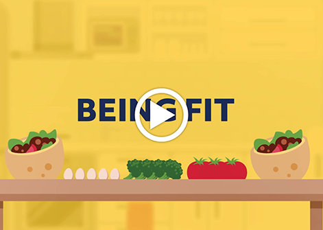 A yellow background with a brown dinner table in front, covered in delicious foods like pita sandwiches and salad, with black block letters over top that say 'being fit'