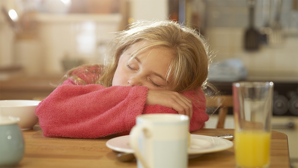 Girl looking too tired to eat the food on the table