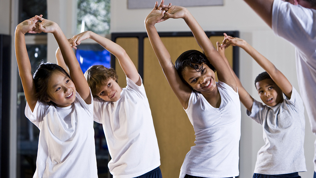 Group of kids standing and stretching in a gym